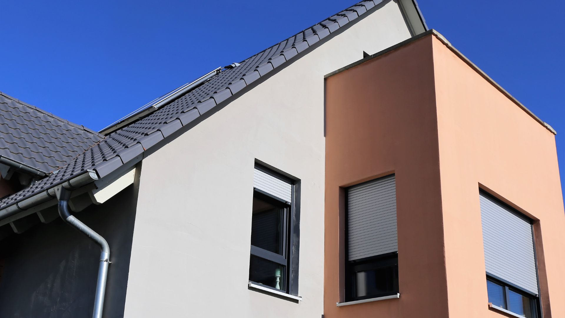 Modern house with white and peach walls, black roof, and roller shutters