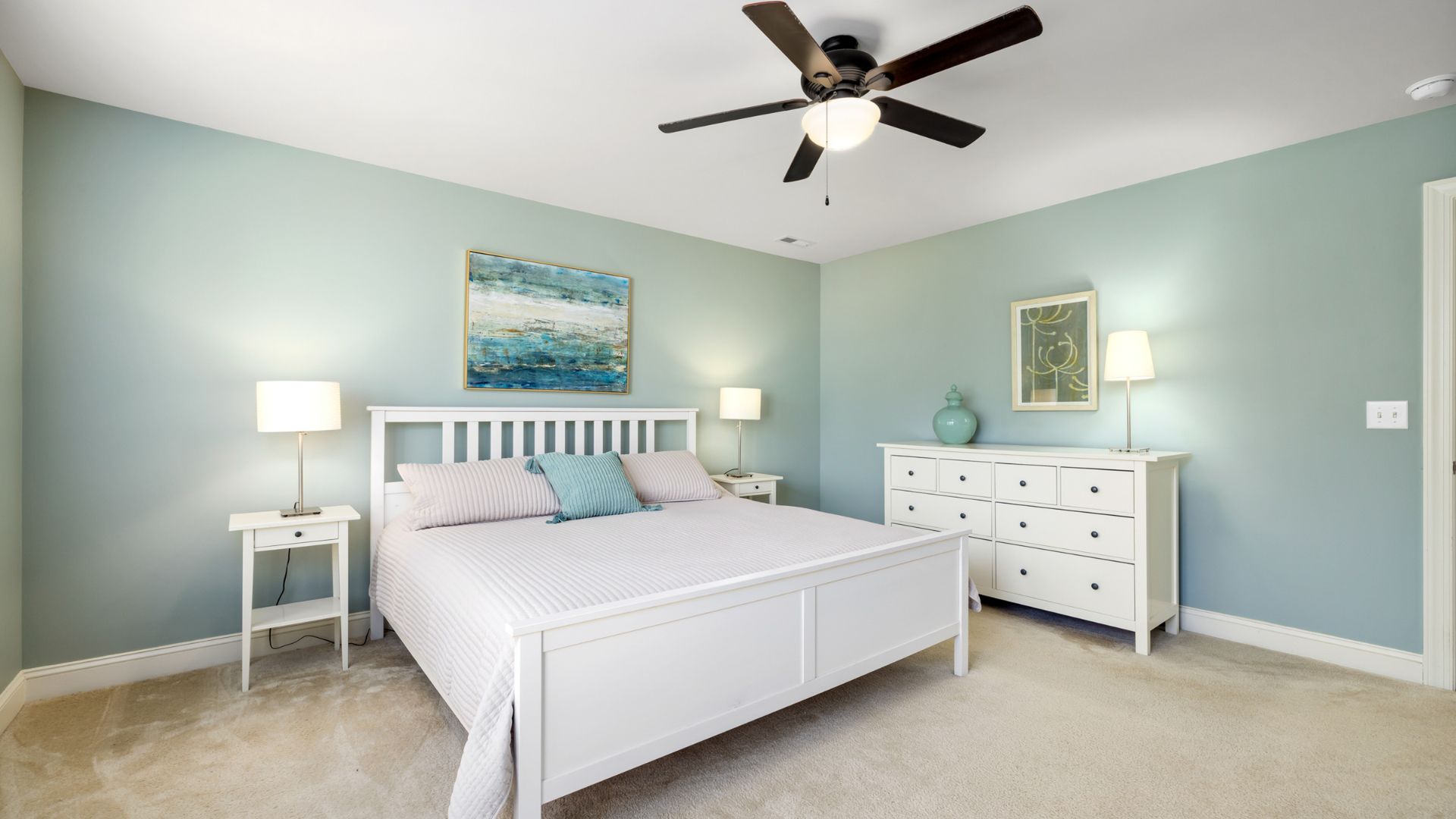Serene bedroom with white furniture, blue walls, and ocean-themed artwork