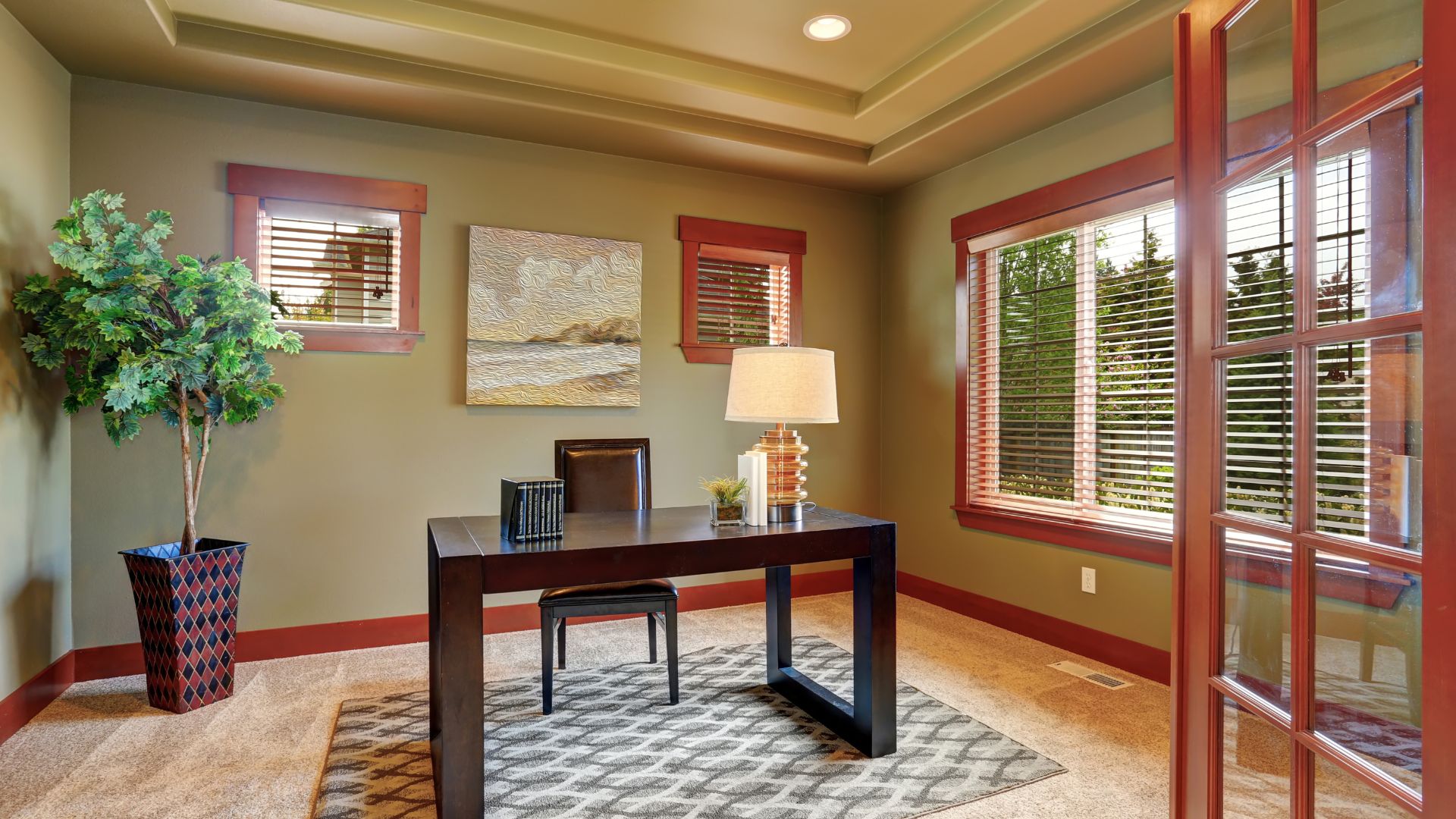 Modern home office with dark wood desk, potted plant, and large windows