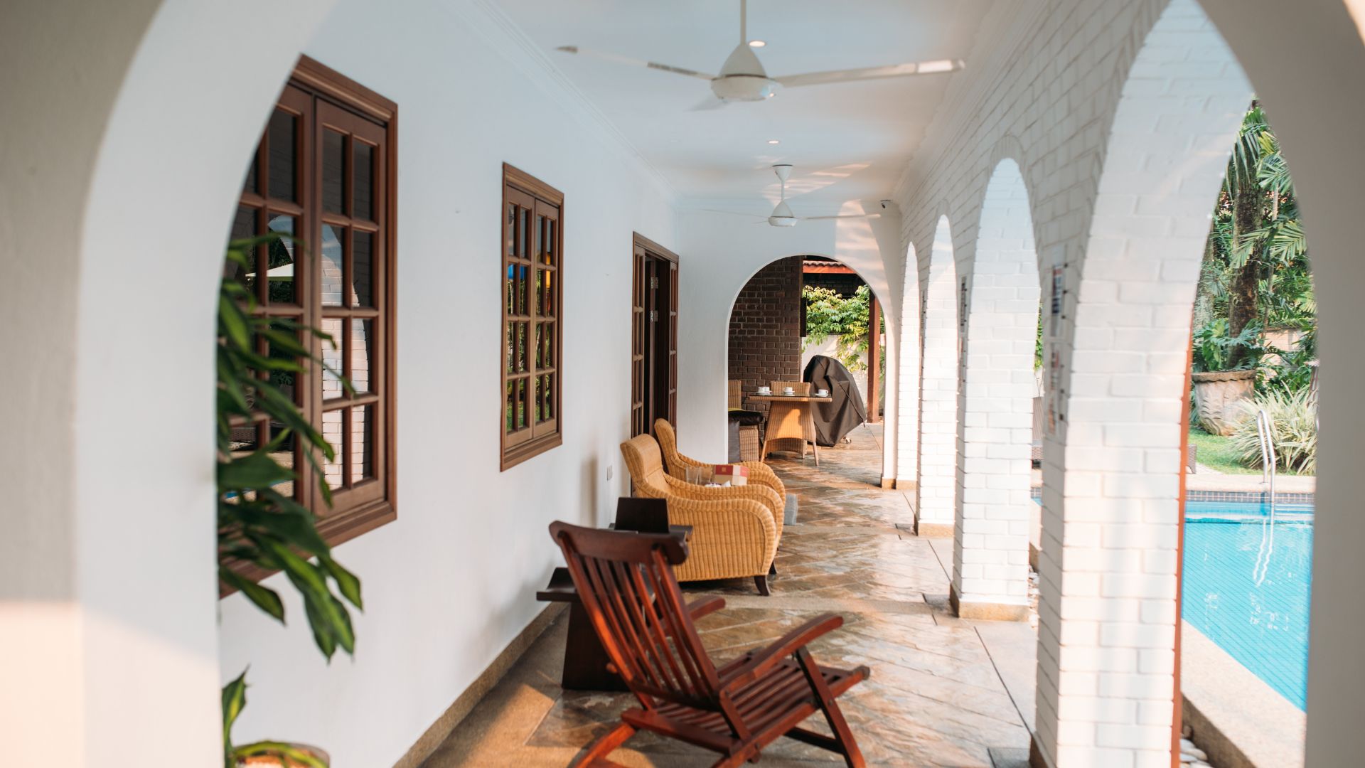 Serene poolside patio with arched walkway, wicker chairs, and white walls