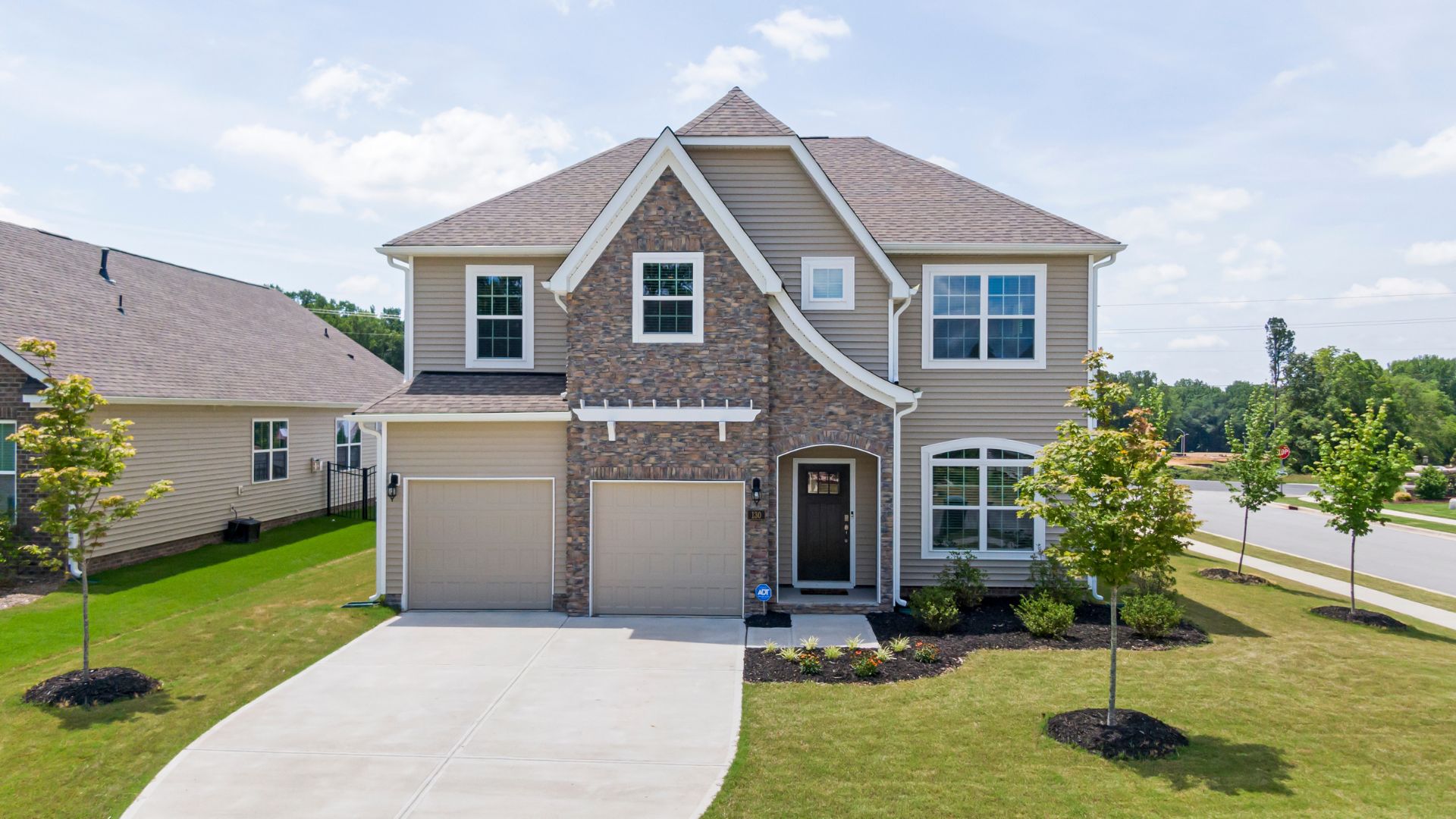 Two-story suburban house with stone facade and double garage on sunny day