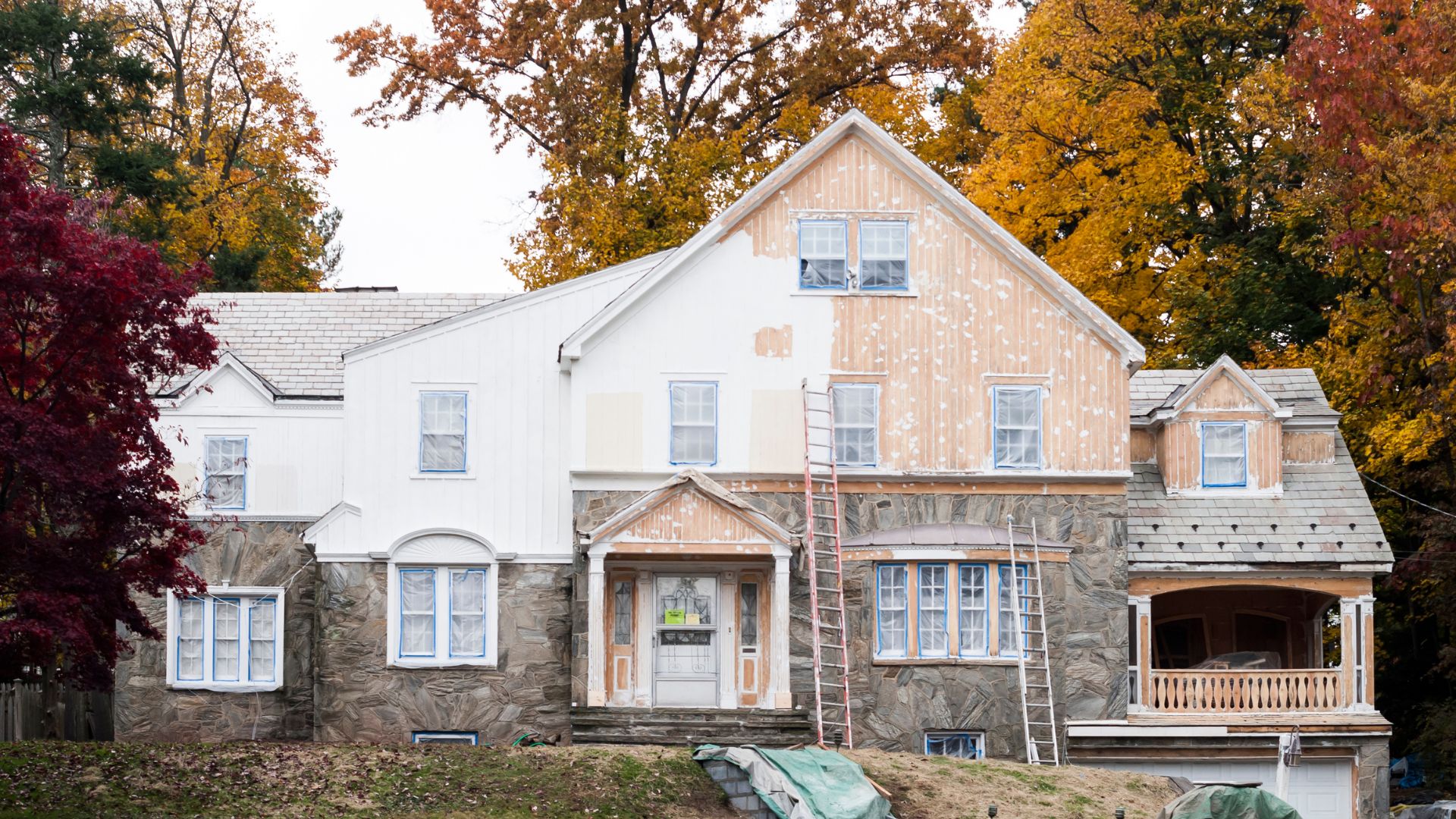 House under renovation with autumn trees and ladder in colorful fall setting