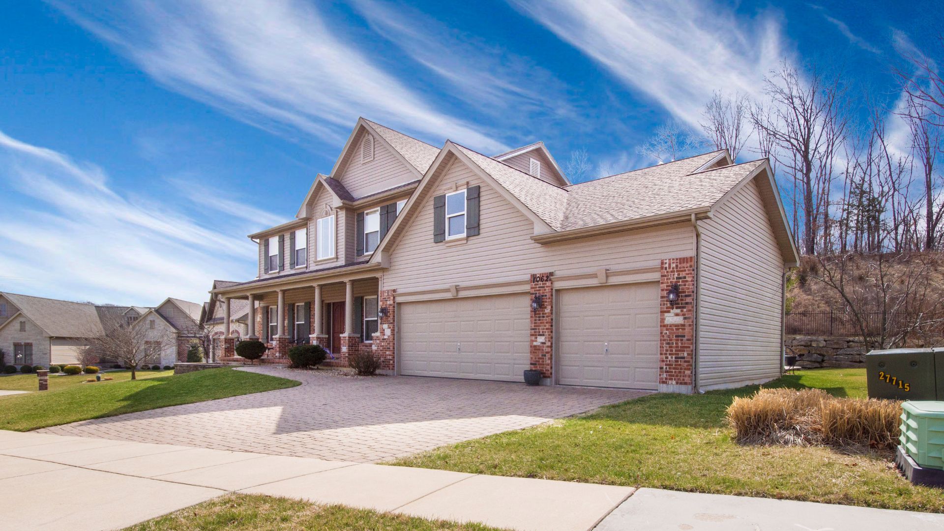 Two-story suburban house with brick accents and three-car garage on sunny day