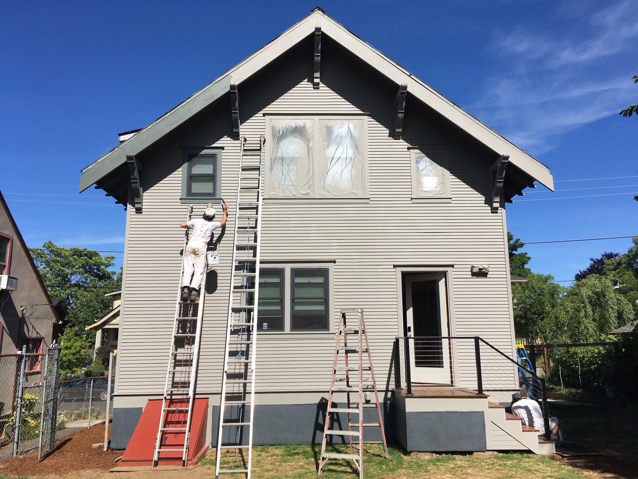 Worker on ladder painting exterior of white two-story house on sunny day