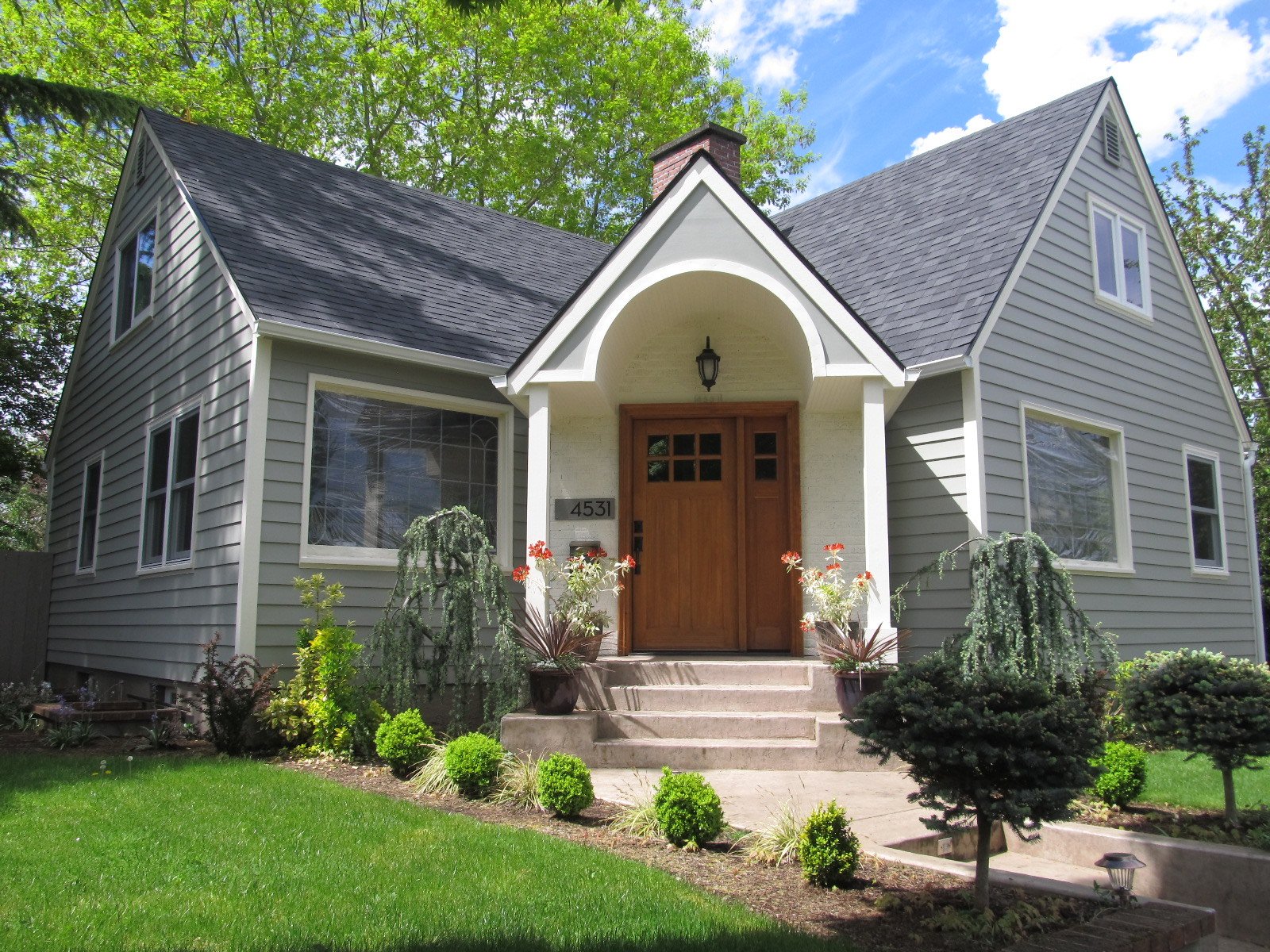 Charming gray house with wooden door, arched porch, and manicured landscaping